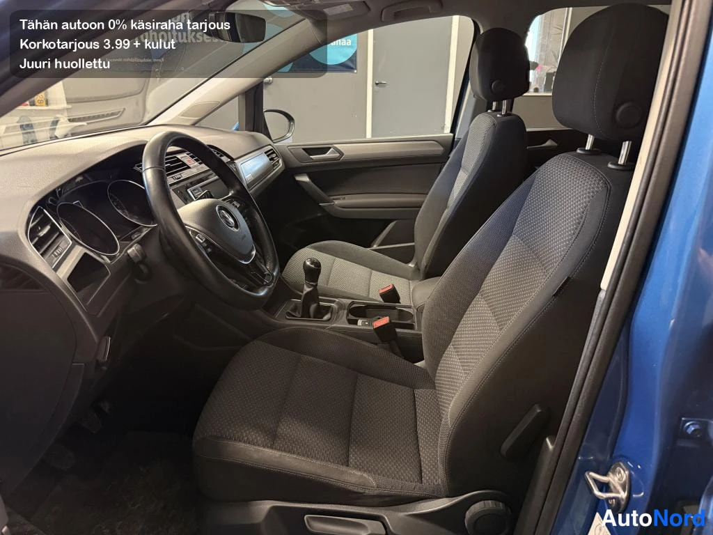 Muu: Volkswagen Touranin etusompelu: kankaaverhoillut etuistuimet, multitoimippa ja käsijarru näkyvät avoimesta ovesta.