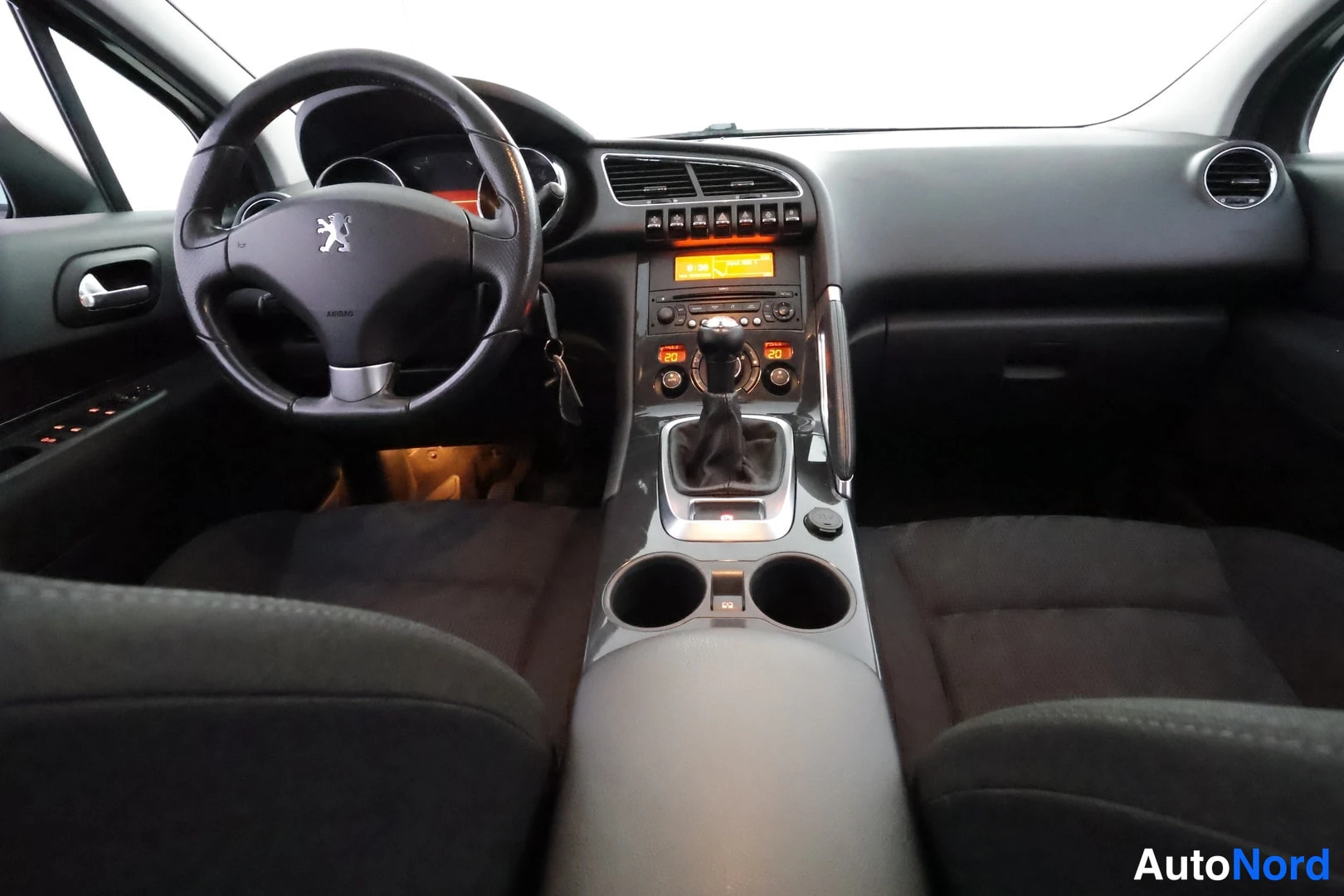 Yksityiskohta: Etukuva kojelautaan: Peugeot-ohjauspyörä, manuaalivaihteen vipu ja radio keskikäytävällä, tummat istuimet.