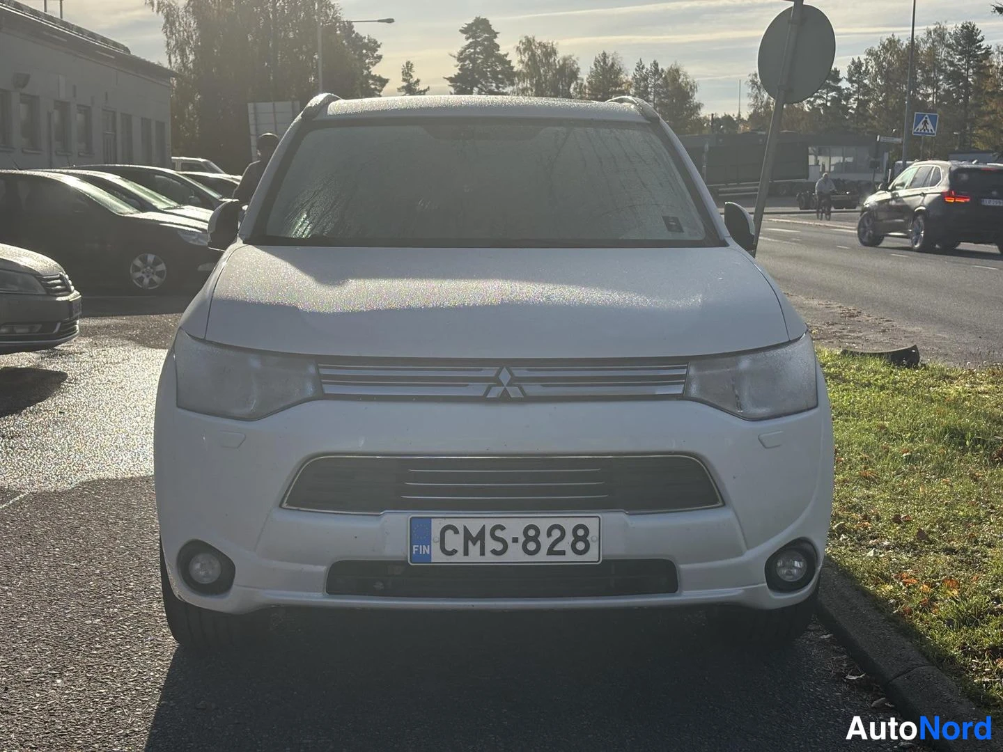 Edestä: Valkoisen Mitsubishi Outlanderin etupää suoraan edestä, rekisterikilpi, tuulilasi sumuisenkostea.