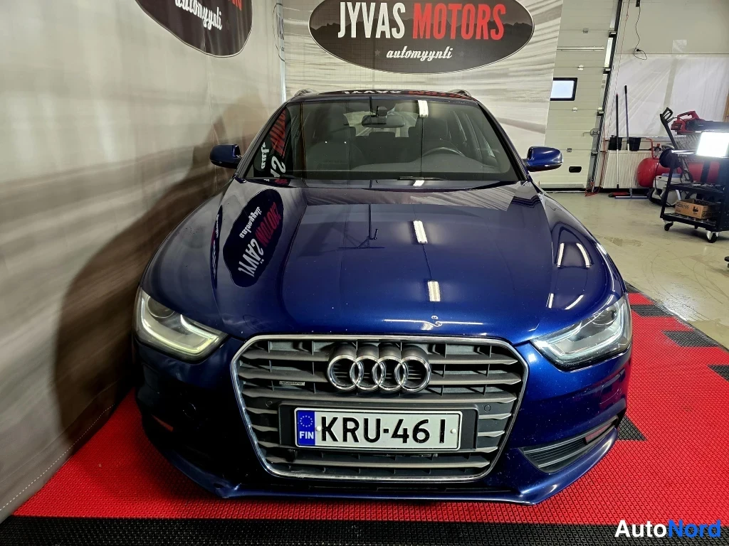 Edestä: Sininen Audi A4 Avant edestä kuvattuna, etusäleikkö ja Audi-merkki näkyvät, rekisterikilpi.