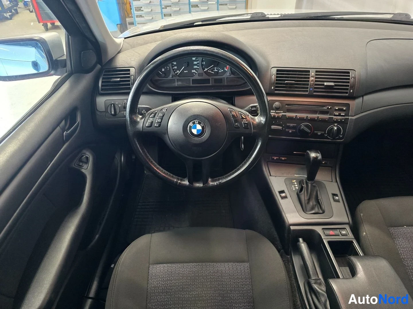 Muu: Auton sisätila kuskinkulmasta: BMW-ohjauspyörä, mittaristo, automaattivaihteen valitsin ja keskikonsolin radiopaneeli.