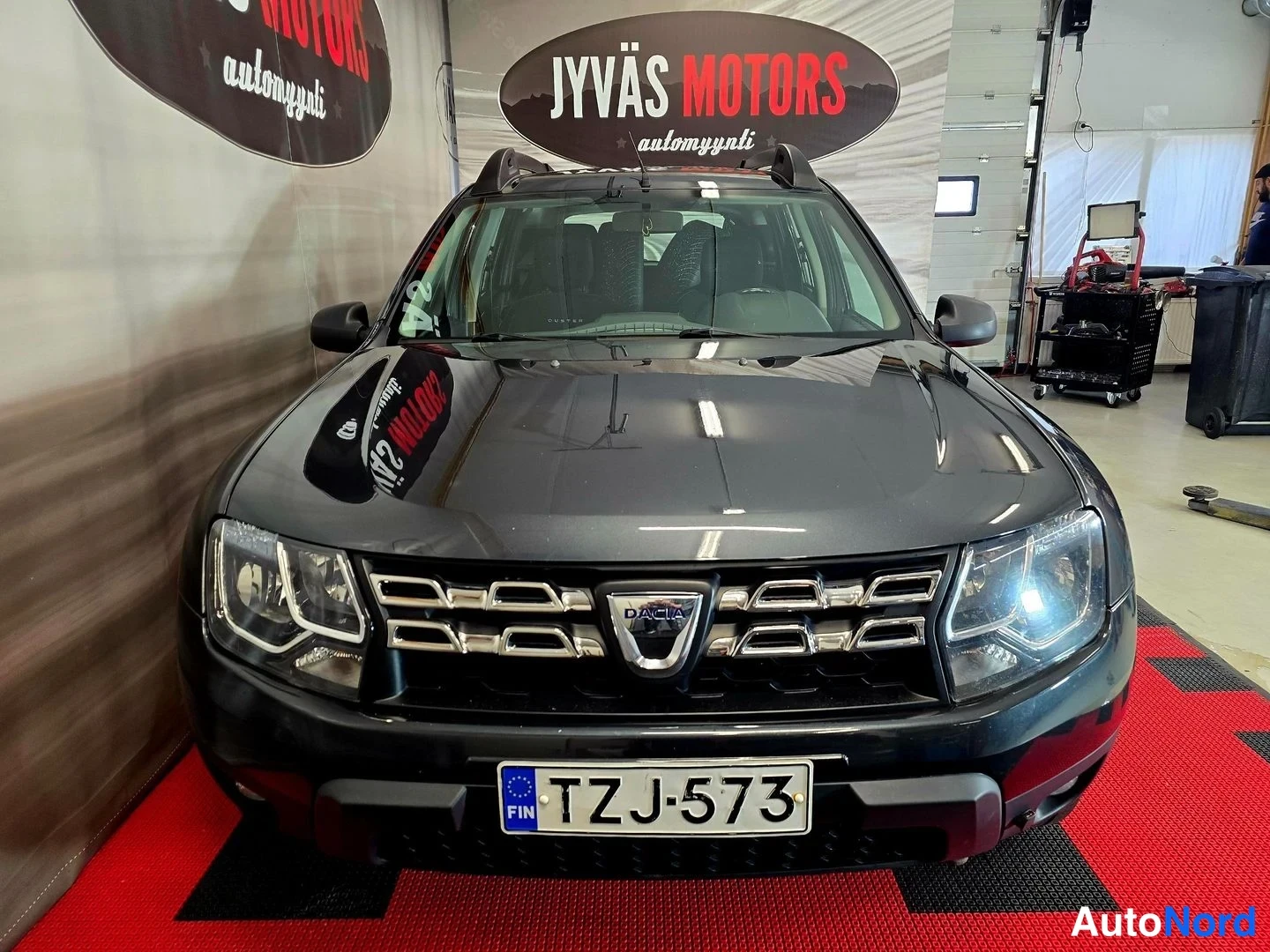 Edestä: Auton etukuva suoraan edestä: tummanharmaa Dacia, rekisteritunnus.