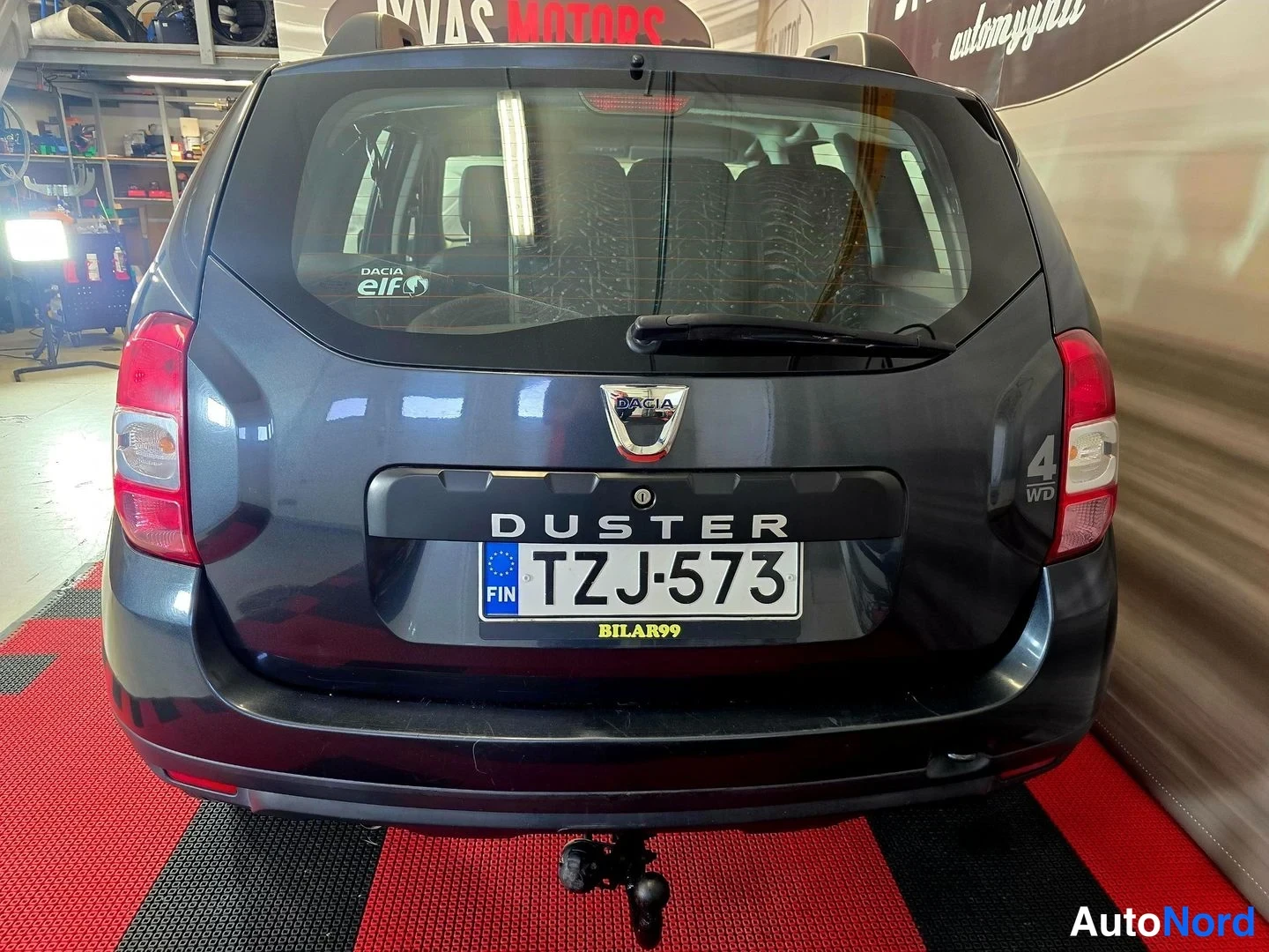 Takaa: Auton takaosa suoraan takaa: tummanharmaa Dacia Duster, rekisteritunnus, Duster-kirjoitus ja Dacia-merkki kannessa, painikkeeton takavalot, veto koukku ja takap