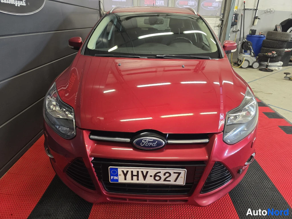 Edestä: Punaisen Ford Focus -farmarin keula etusta: etupuskuri, Ford-merkki grillessä, ajovalot ja rekisterikilpi.