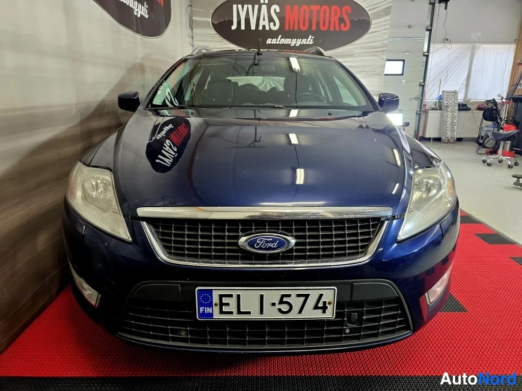 Edestä: Tummansinisen farmariauton etupää suoraan edestä sisätiloissa; Ford-merkki grillessä ja rekisterikilpi.