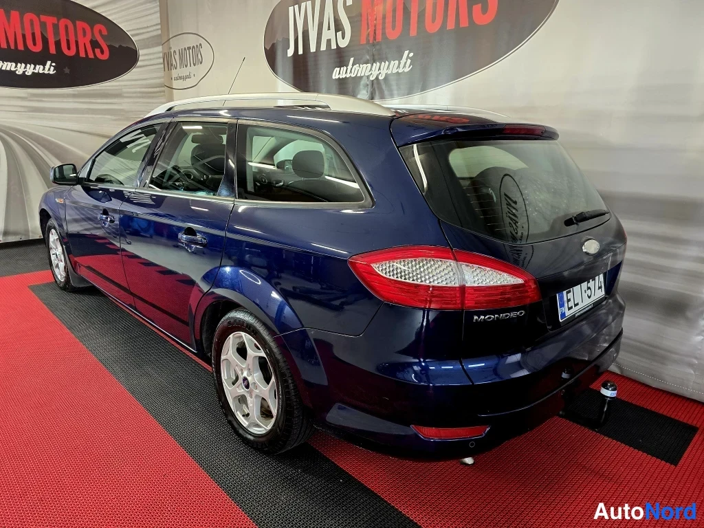Takaviisto: Tummansinisen farmariauton takaosa ja vasen kylki vinosti kuvattuna; näkyvissä takavalot, Mondeo-teksti, kattokaiteet ja valokatkaisin vetokoukussa.