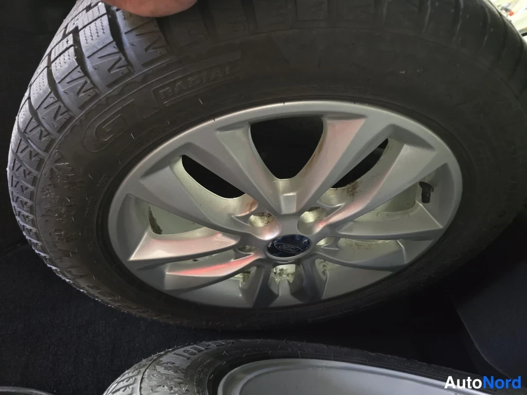 Yksityiskohta: Yksityiskohta Ford-henkilon cabrioletin/mondeon?: alumiinivannettä renkaaseen kiinnitettynä; Ford-merkki; vanne pölyinen.