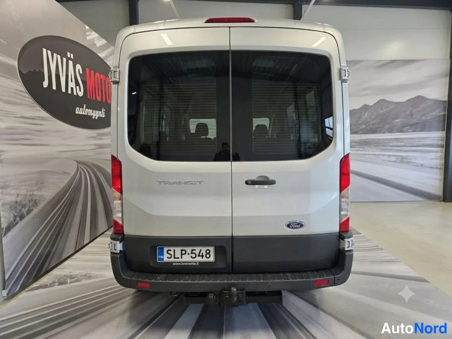 Takaa: Pakettiauto suoraan takaa nähtynä sisätiloissa, rekisterikilpi, vetokoulu takana.