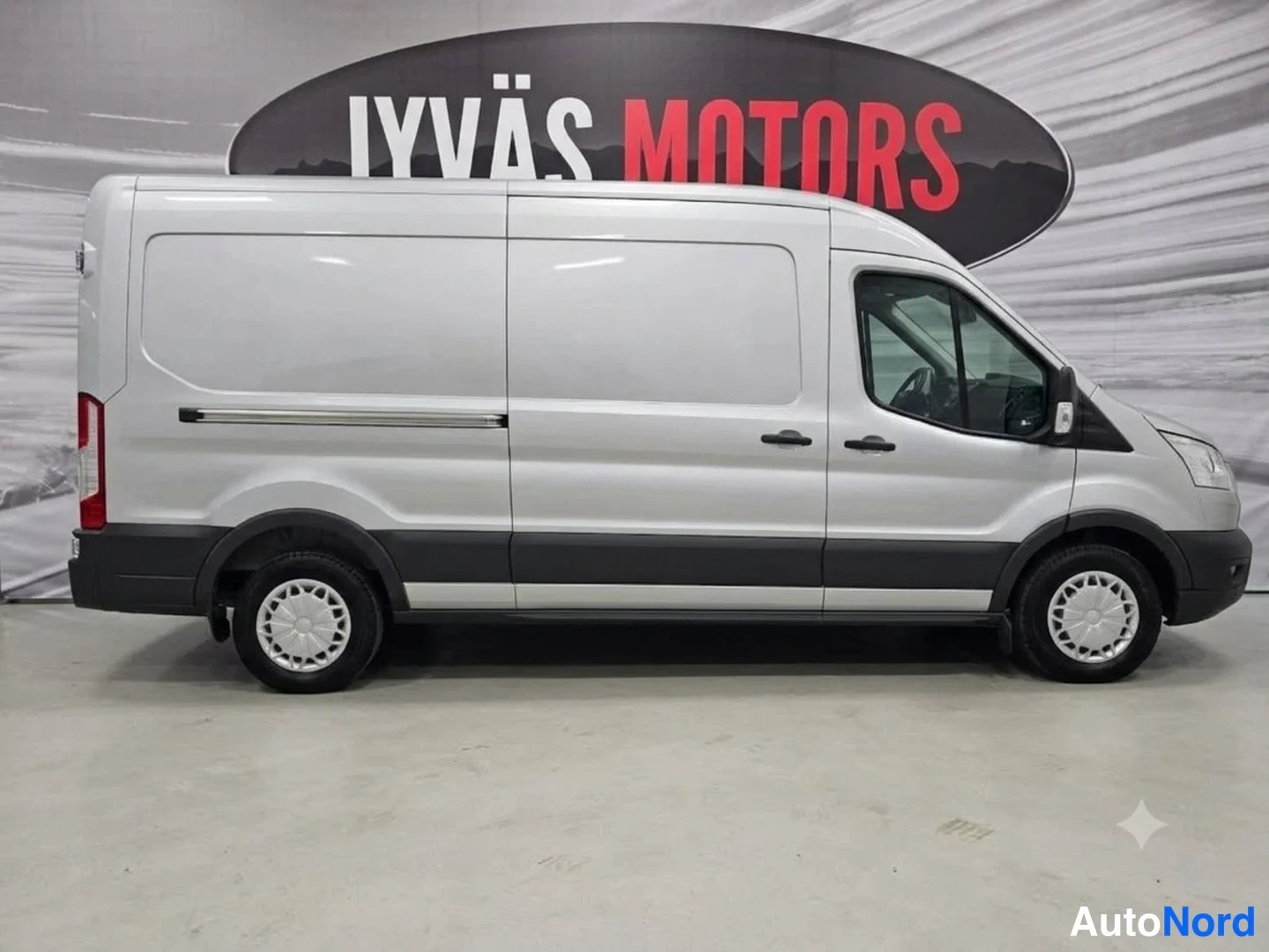 Etuviisto, nokka oikealle: Hopeanharmaa Ford Transit -pakettiauto sivulta etukulmasta sisätiloissa