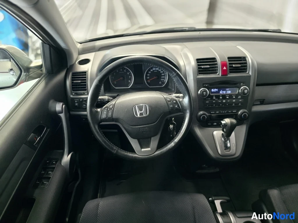 Sivulta: Honda CR-V:n kojelauta suoraan ohjaamosta kuvattuna: ohjauspyörä Honda-merkillä ja monitoimapainikkeilla, analogiset nopeus- ja kierrosmittarit, keskirivissä ää