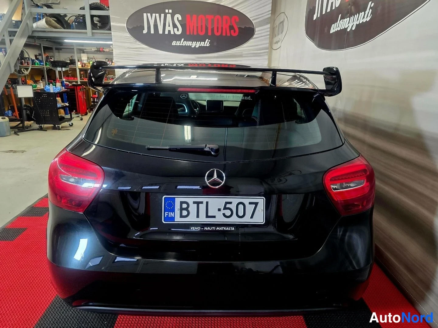 Takaa: Mustan Mercedes-Benz -henkilöautin takanäky: suuri musta takasiipi, punaiset takavalot ja rekisterikilpi.