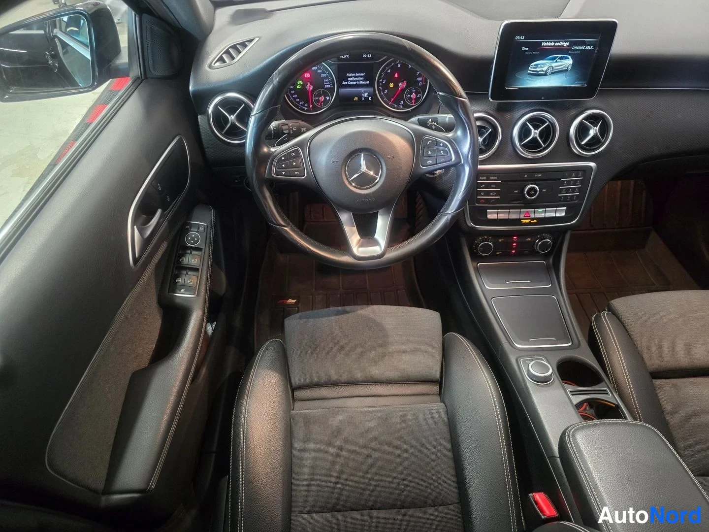 Yksityiskohta: Mercedes-Benz -henkilöautin etuosan sisätilat: Mercedes-merkitty ohjauspyörä, mittaristo, näyttö ja hallintalaitteet.