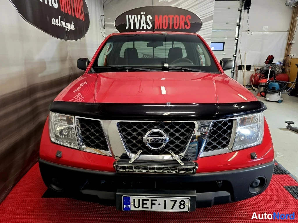 Edestä: Punaisen Nissan Navara -mallin suora etukuva sisätiloissa, rekisteritunnus.