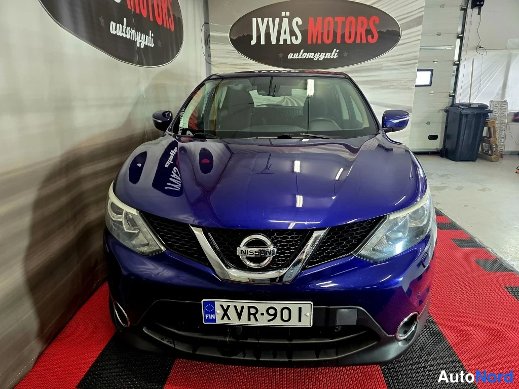 Edestä: Sinisenä tummansininen Nissan Qashqai seisoo etuosasta suoraan kohti kameraa Autoliike Jyväs Motorsin tiloissa; etusäleikkö, Nissan-merkki ja rekisterikilpi näk
