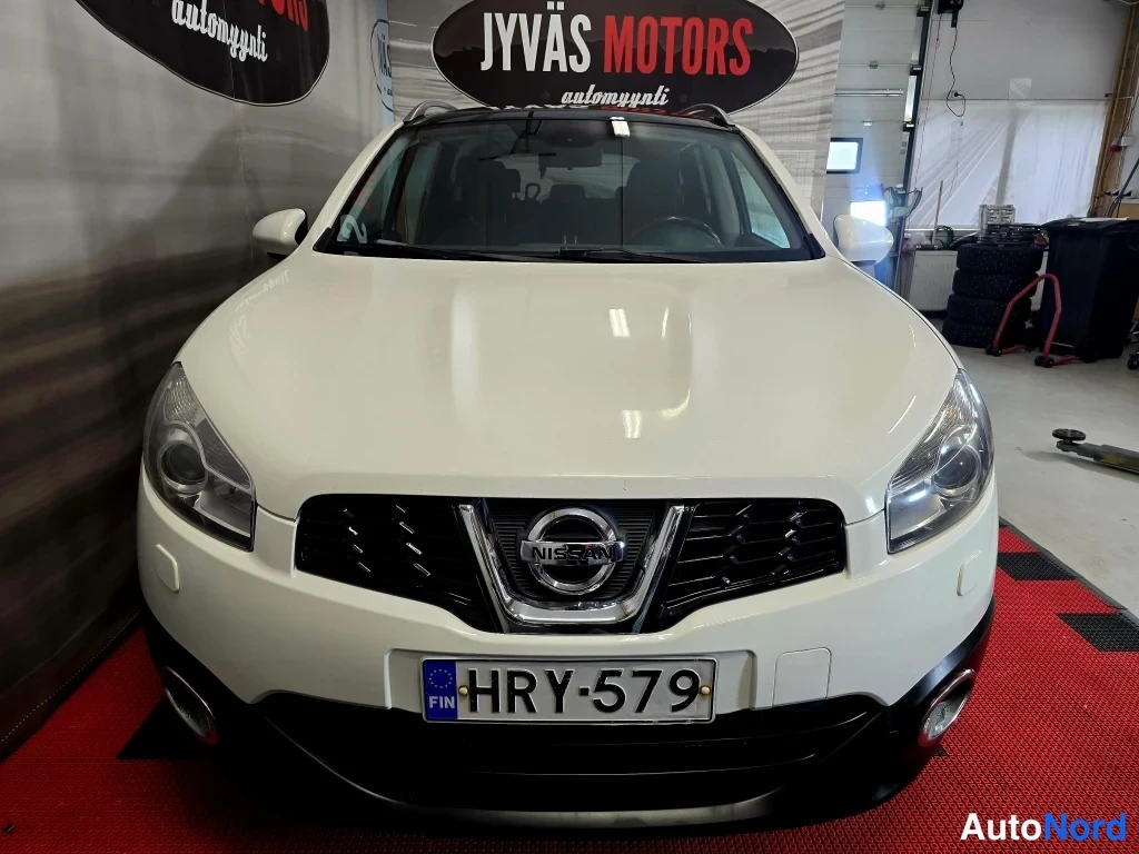 Edestä: Nissan Qashqai+2 etupää suoraan edestä, valkoinen koripelti, musta etusäleikkö Nissan-merkillä ja rekisteri.