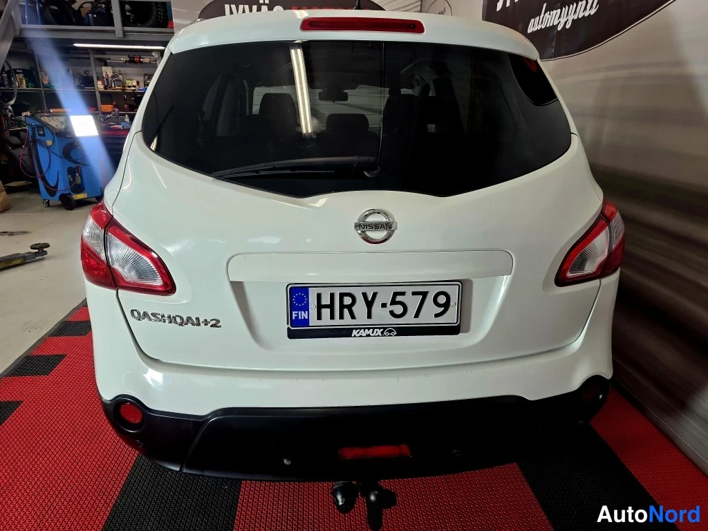 Takaa: Nissan Qashqai+2 takapää suoraan takaa, valkoinen koripelti, QASHQAI+2-teksti, Nissan-merkki ja rekisteri, vetokoukku näkyy alhaalla.