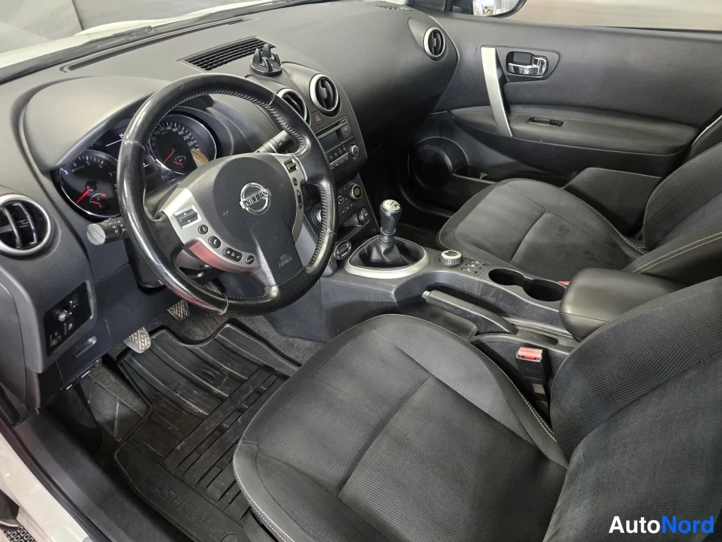 Muu: Nissan Qashqai+2 kuljettajan näkymä, manuaalivaihteisto ja Nissan-logo ratti on näkyvissä.