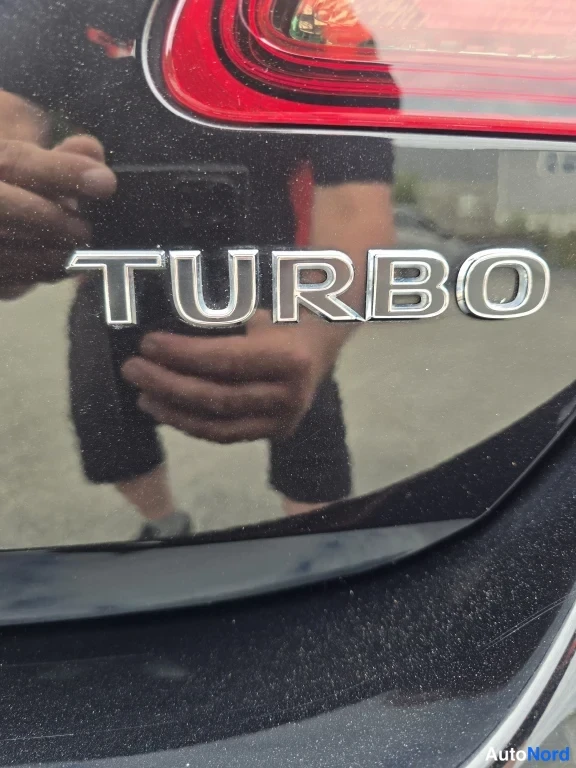 Yksityiskohta: Tarkennus mustasta autosta, jossa on kromattu TURBO-merkintä takavalojen välissä.