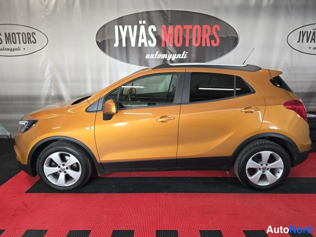 Sivulta: Oranssi Opel Mokka X sivusta vasemmalta katsottuna sisätiloissa, taustalla Jyväs Motors -banneri.