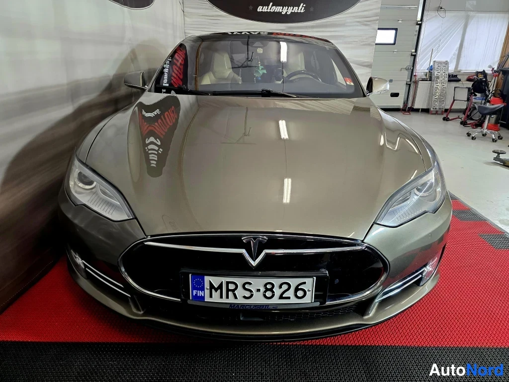 Edestä: Tesla Model S -sedanin etupää kuvattu suoraan edestä sisätiloissa; konepelti, etusäleikkö ja Tesla-merkki näkyvät, rekisterikilpi.