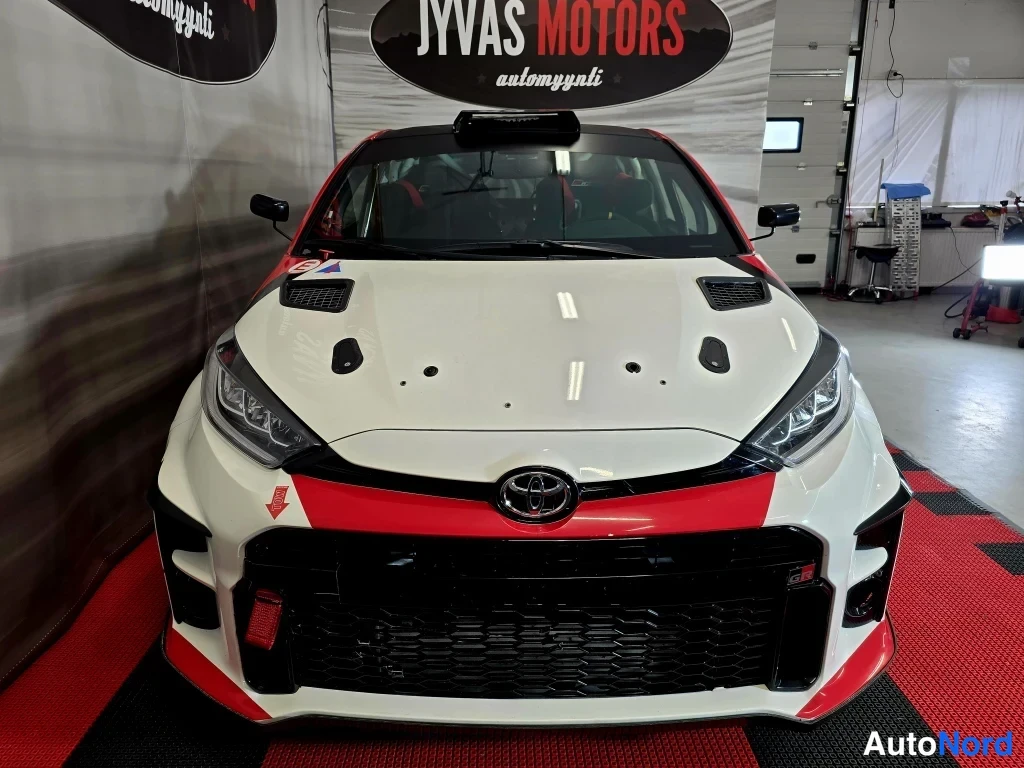 Edestä: Toyota Yaris -ralliauto suoraan edestä, valkoinen punamustalla keulalla ja suurella mustalla etugrilla.