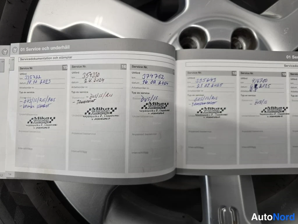 Yksityiskohta: Avoin Volvo-huoltokirja sivulla '01 Service och underhåll', käsinkirjoitetut huoltomerkinnät ja Mika Automo-huoltoliikkeen leimat, taustalla hopeinen aluvanne.