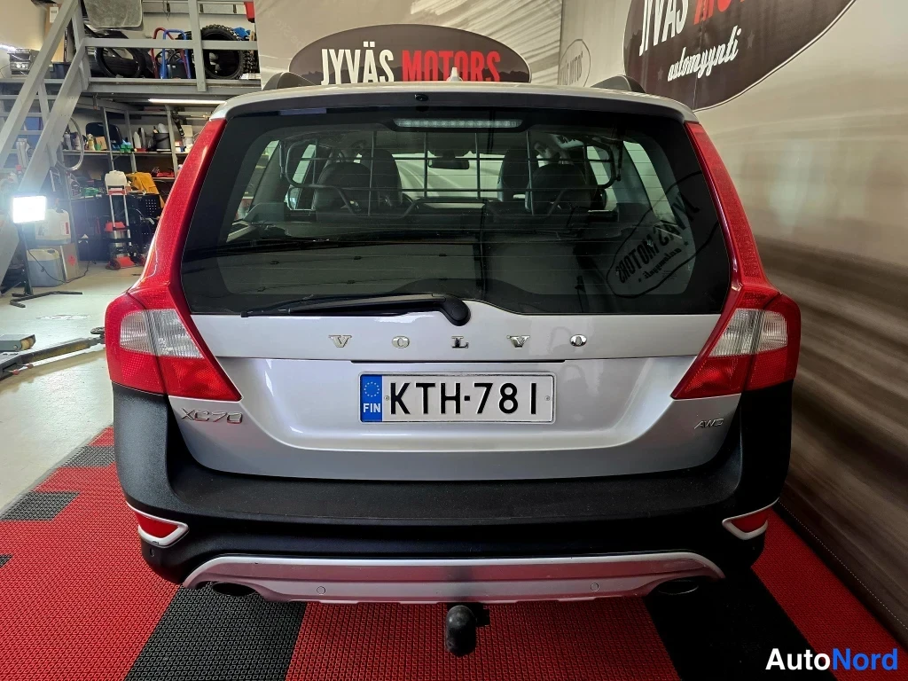 Takaa: Auton takaosa suoraan takaa: hopea Volvo XC70 -farmari, rekisterikilpi, XC70- ja AWD-merkinnät, kattokaiteet ja vetokoukku.