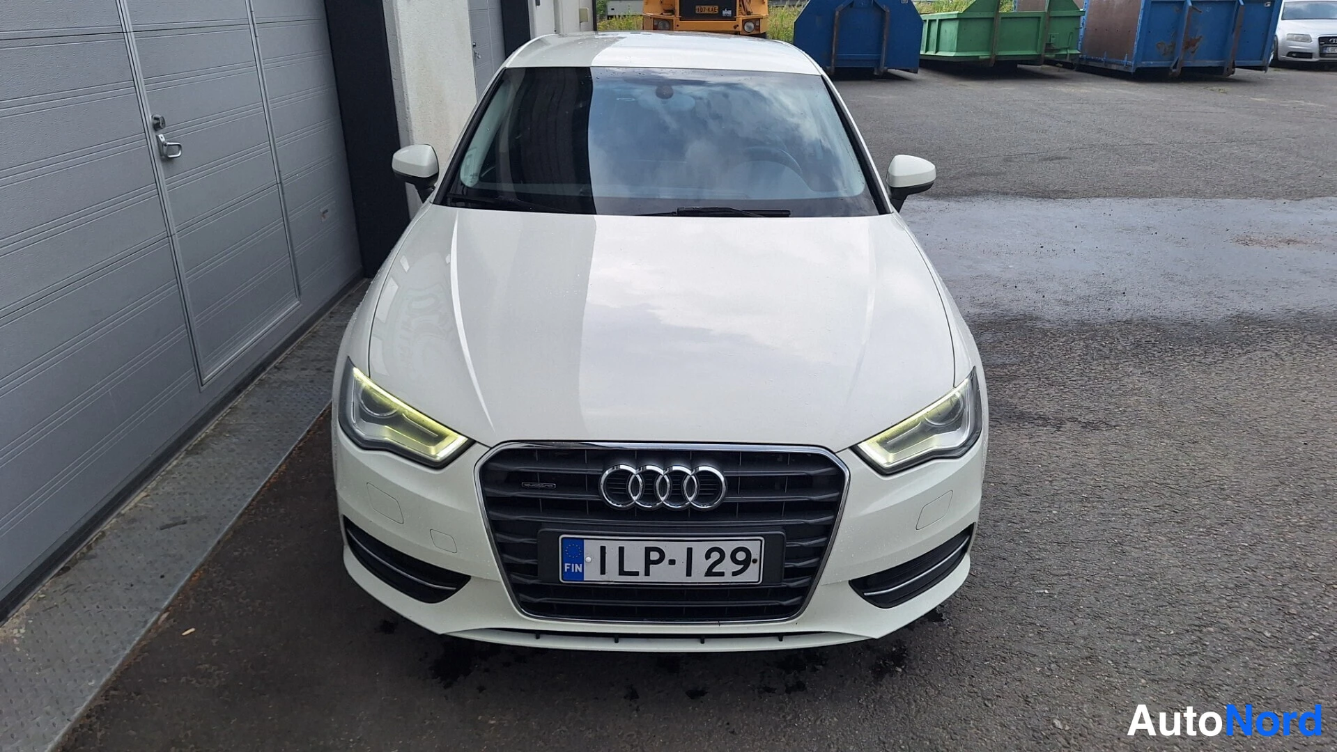 Edestä: Valkoisen Audi A3 Sportbackin etunäkymä suoraan edestä, rekisterikilpi näkyvissä.