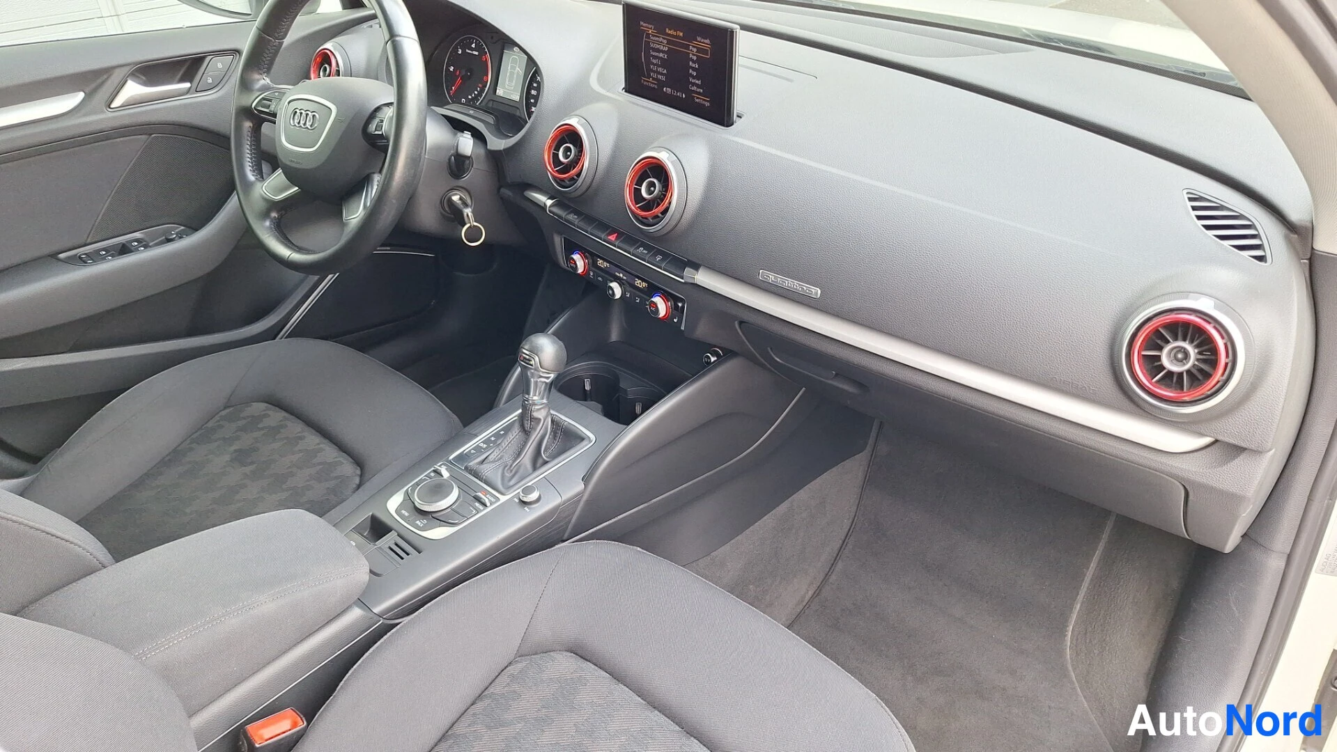 Muu: Audi A3:n sisätila: ohjauspyörä, mittaristo, MMI-näyttö, tumma kojelauta ja kangasistuimet.