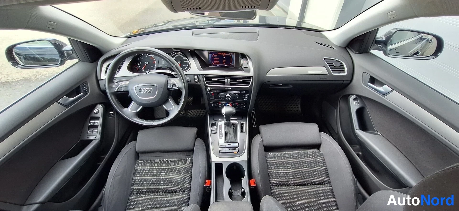 Muu: Auton ohjaamo ylhäältä: Audi-ohjauspyörä, kojetaulu, infotainment-näyttö, automaattivaihteen valitsin ja kaksi etuistuinta.