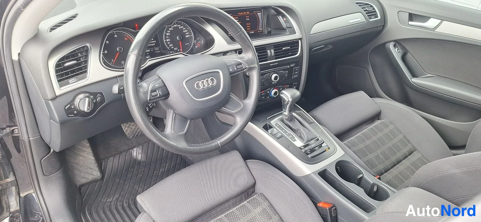 Muu: Audi-nelospyörän ohjaamo näkyvät kuvassa ohjauspyörä, mittaristo, automaattivaihteen valitsin, keskikonsoli ja kaksi kangasistuinta.