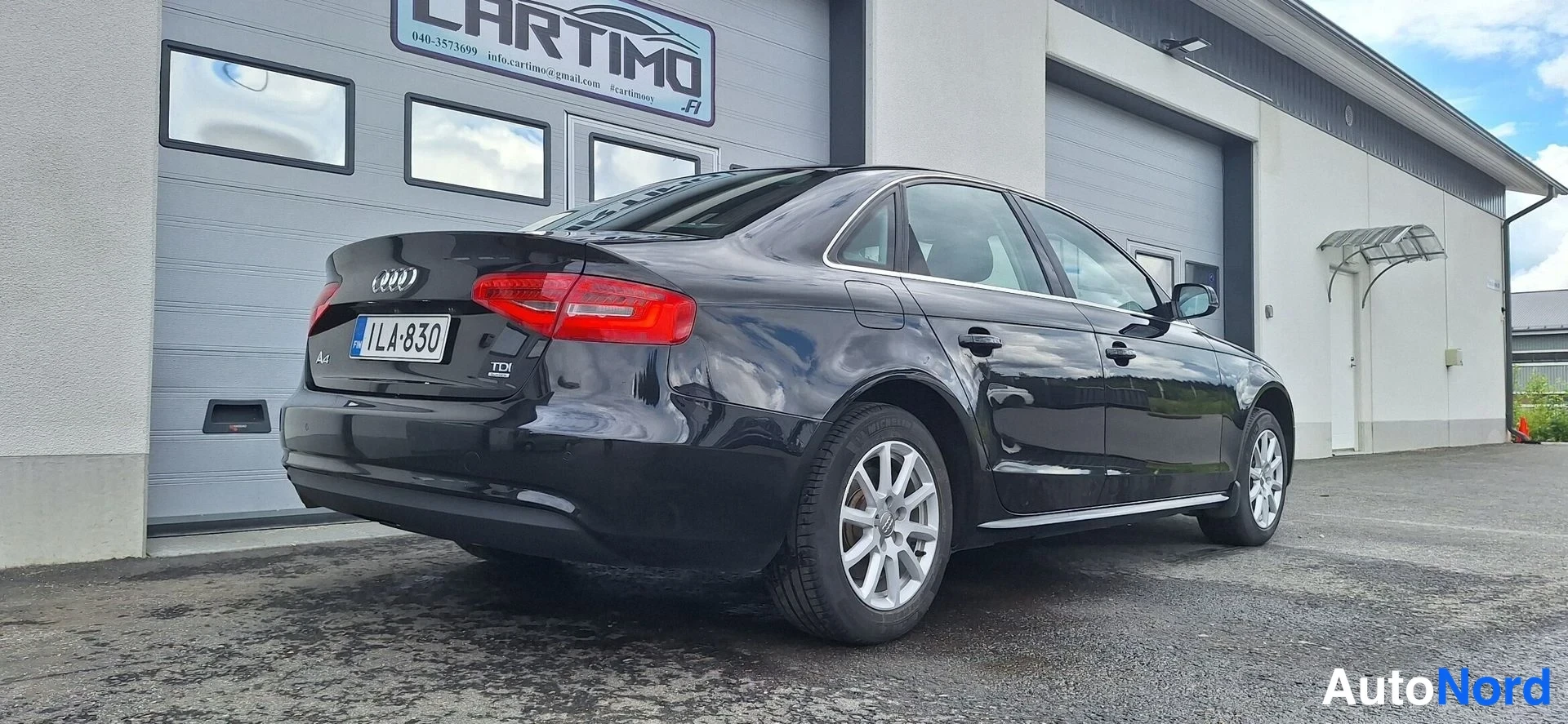 Takaviisto: Mustan Audi A4 -sedanin takakulma, rekisteritunnus, autotallin ovella.