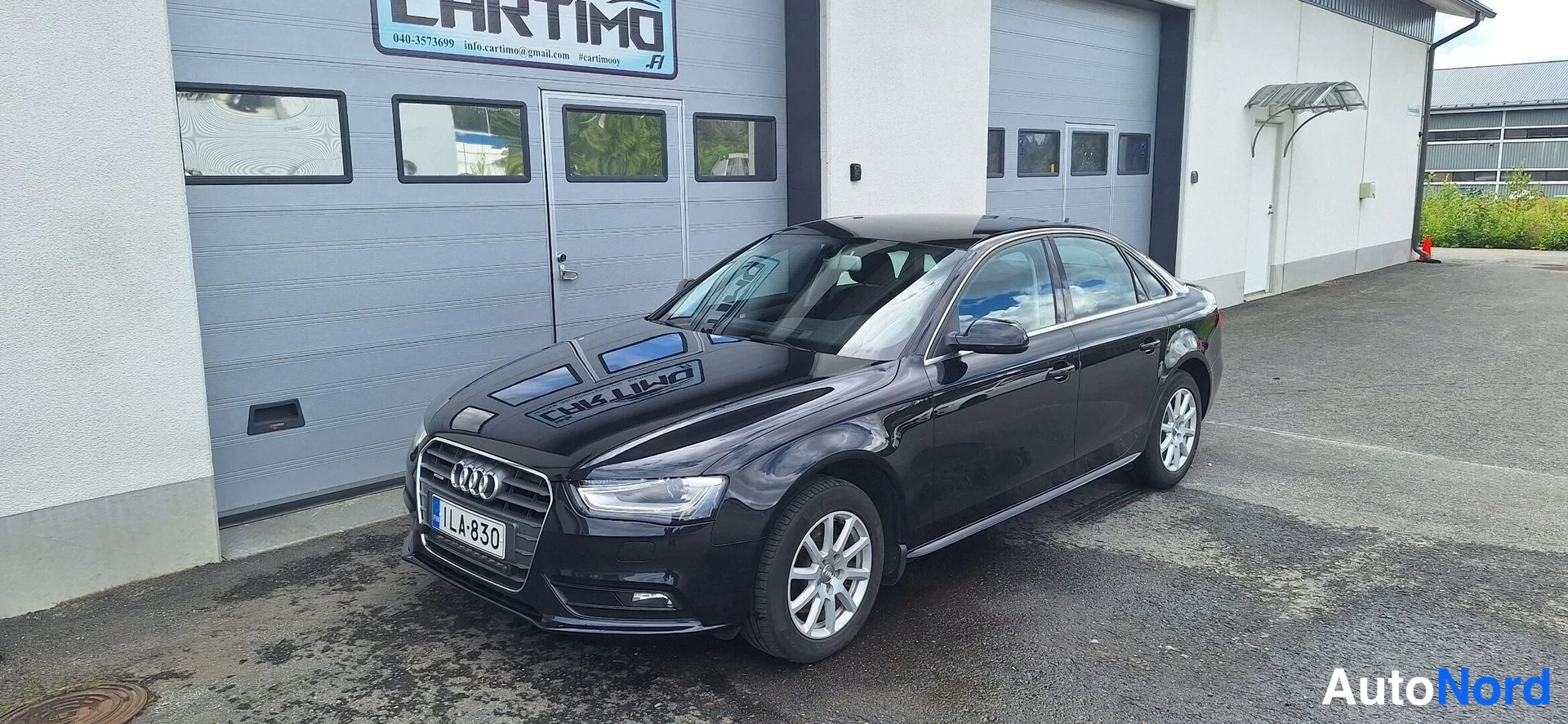 Etuviisto, nokka vasemmalle: Audi A4 -sedanin etukulmakuva: musta runko, etugrilli ja ajovalot näkyvät vasemmalla, kylki autotallin ovien edustalla.