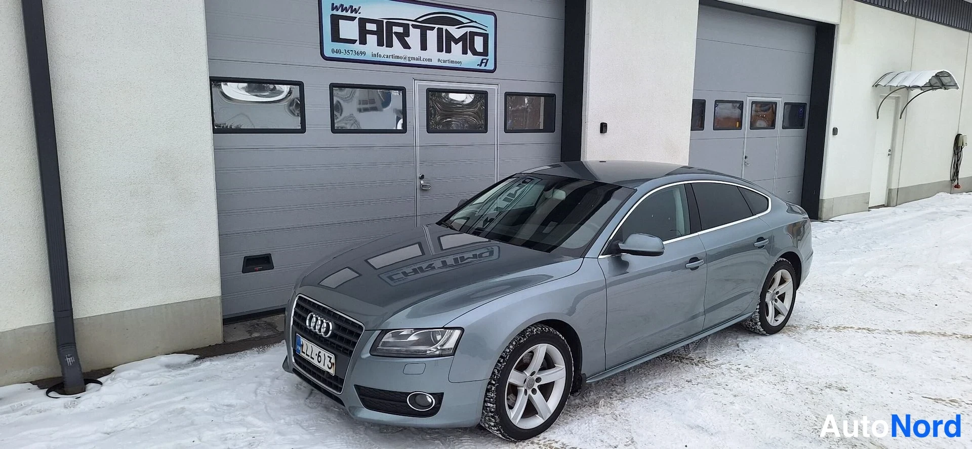 Etuviisto, nokka vasemmalle: Audi A5 Sportback etukulmasta, keulakorsi ja etupyörä näkyvät, harmaa kori, lunta maassa, rekisteri LL-613.