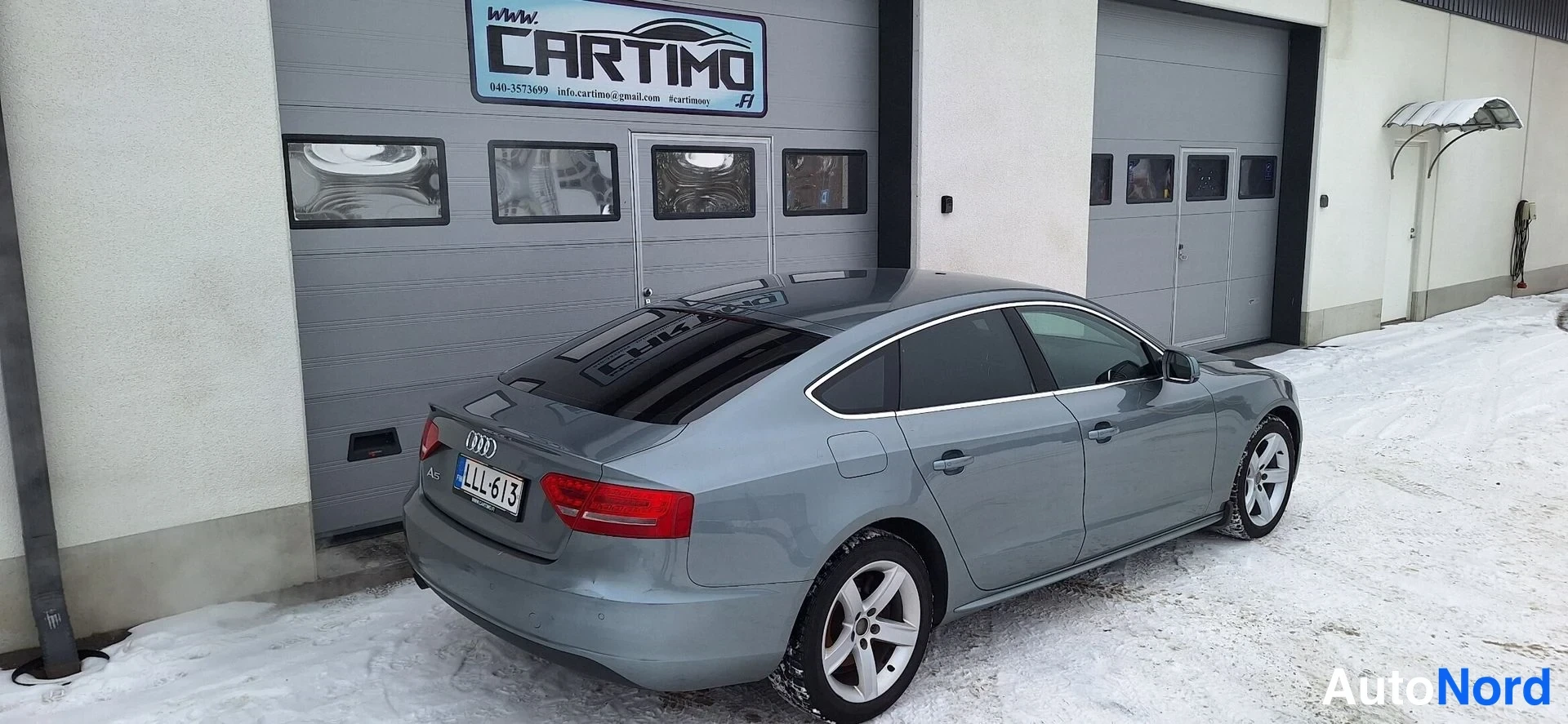Takaviisto: Audi A5 Sportbackin takaosaa ja vasenta kylkeä lumisella pihalla, rekisterikilpi.