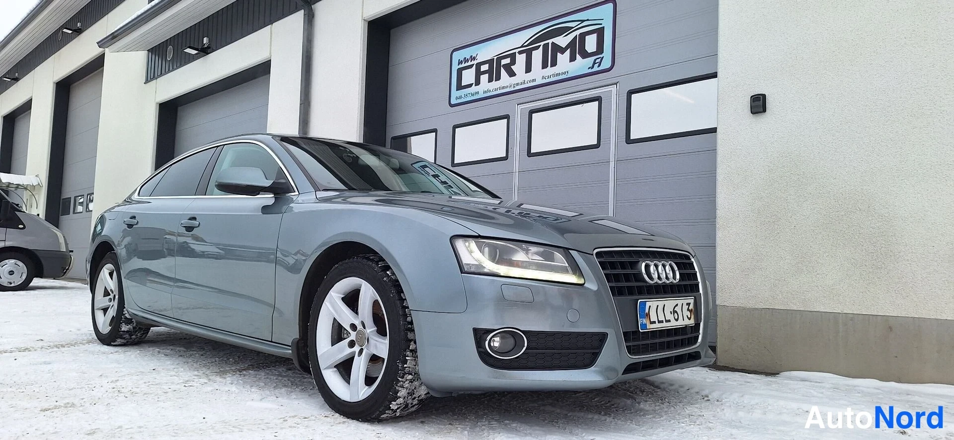 Etuviisto, nokka oikealle: Audi A5 Sportbackin etukulma lumisella pihalla, harmaankiillokkinen korirakenne