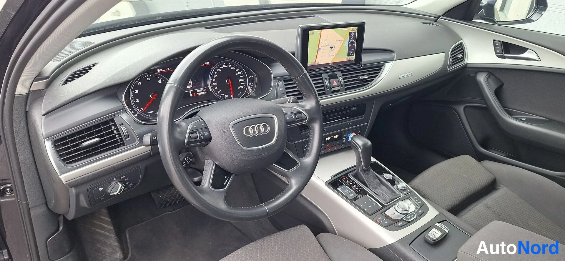 Muu: Ohjaamo näkyvissä: Audi-ohjauspyörä, mittaristo ja keskikonsoli, navigointinäyttö ylhäällä.
