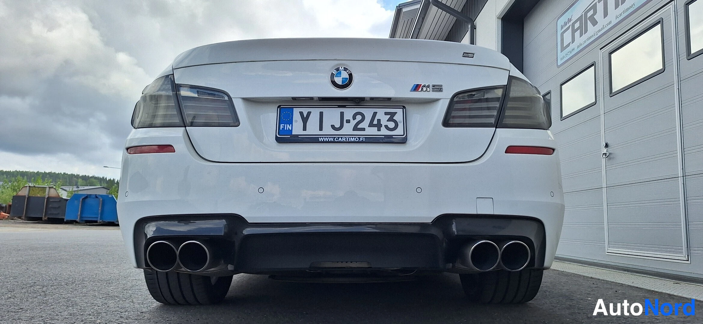Takaa: Valkoisen BMW-sedanin takaosa suoraan takaa, neljä pakoputkea, tummat takavalot ja rekisterikilpi.