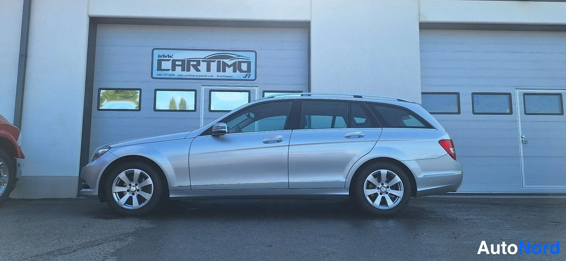 Takaviisto: Hopeanvärinen Mercedes-Benz C -farmari kylki ja takaosa näkyvät, punaiset takavalot oikealla.