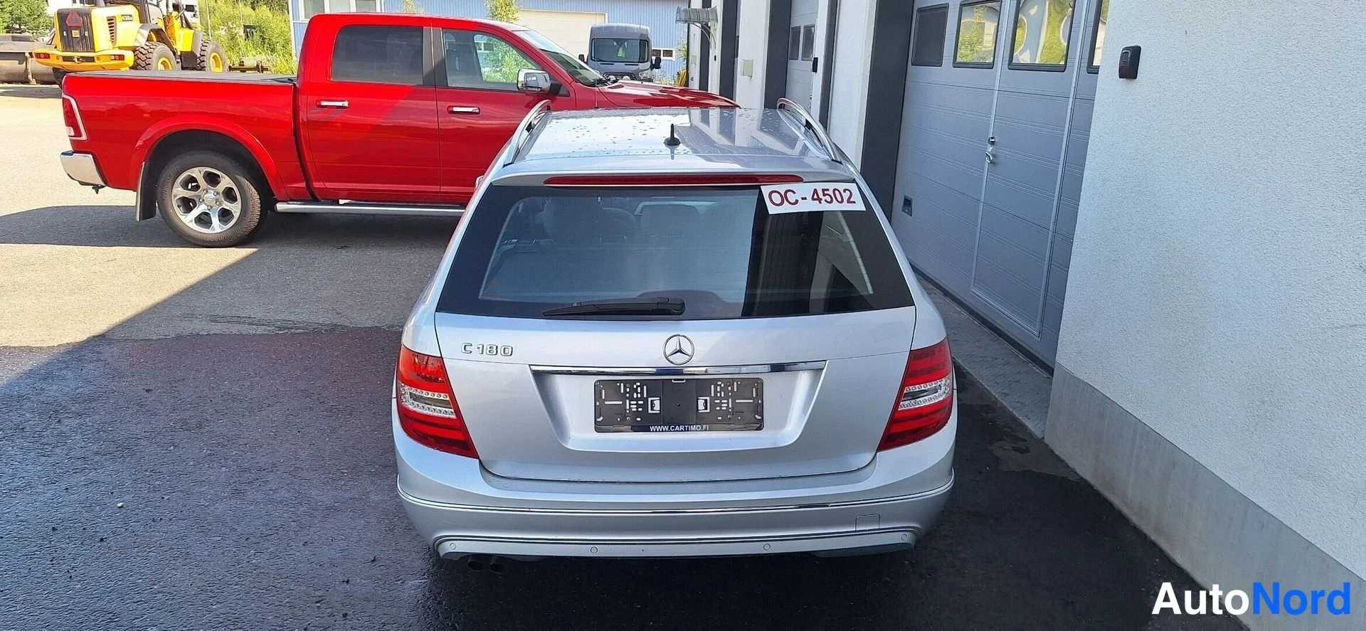 Takaa: Hopeaisen Mercedes-Benz C180 -farmarin takaosa suoraan takaa, takapyyhkijä ja C 180 -teksti takaluukussa, lappu OC-4502 takalasinassa.