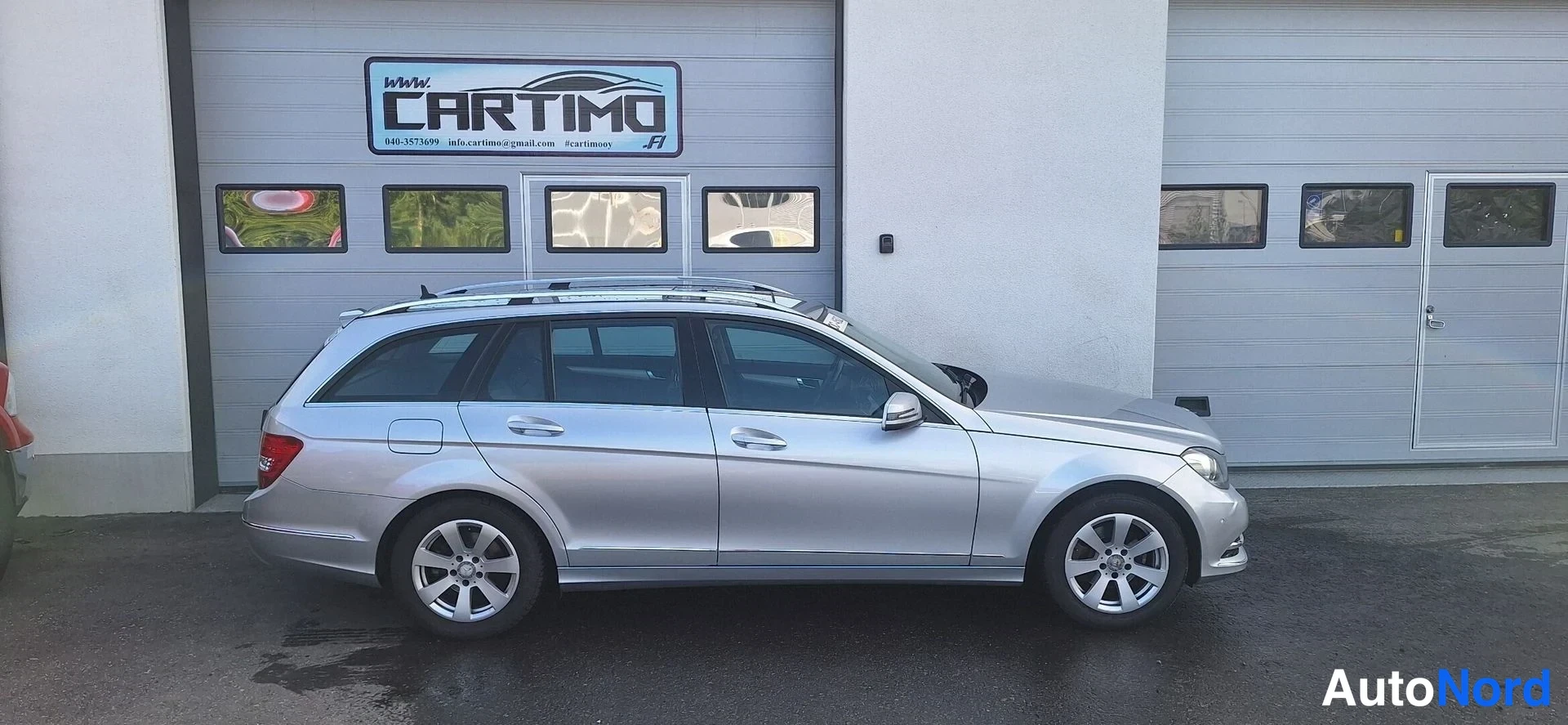 Etuviisto, nokka oikealle: Hopeanvärinen Mercedes-Benz C -farmari sivulta, keulan kohtaus kulmassa.