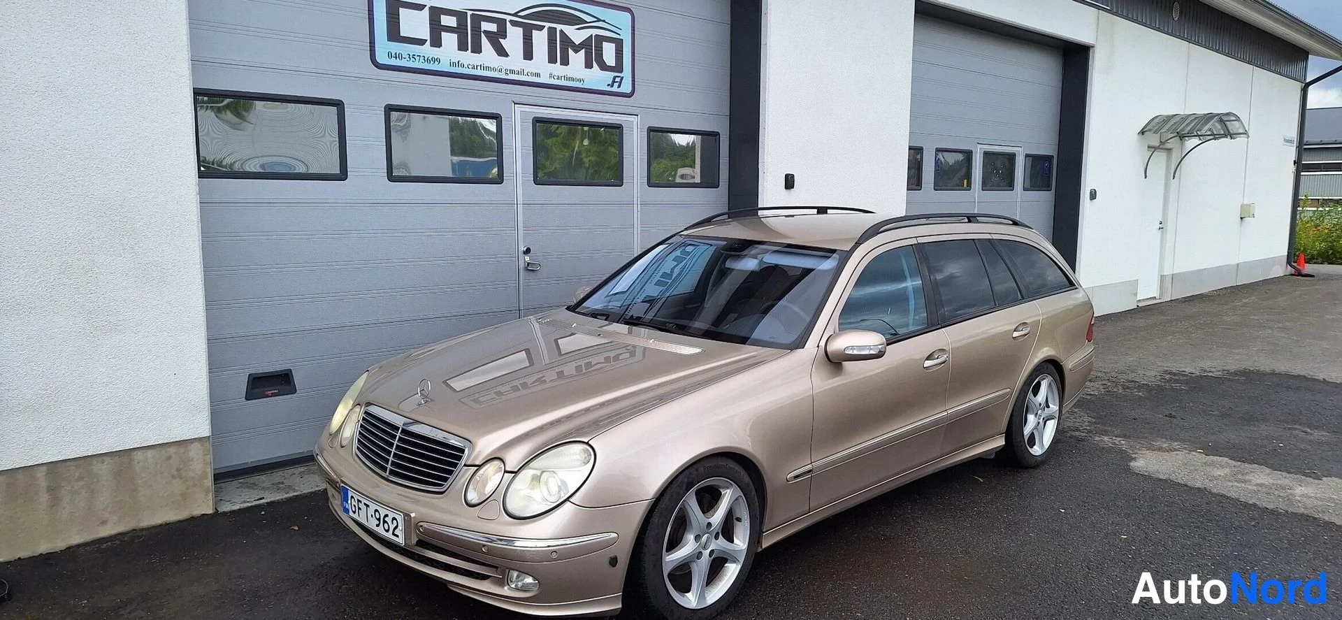 Etuviisto, nokka vasemmalle: Mercedes-Benzin keula vasemmalla, beige farmari parkissa CARTIMO-oven edessä.