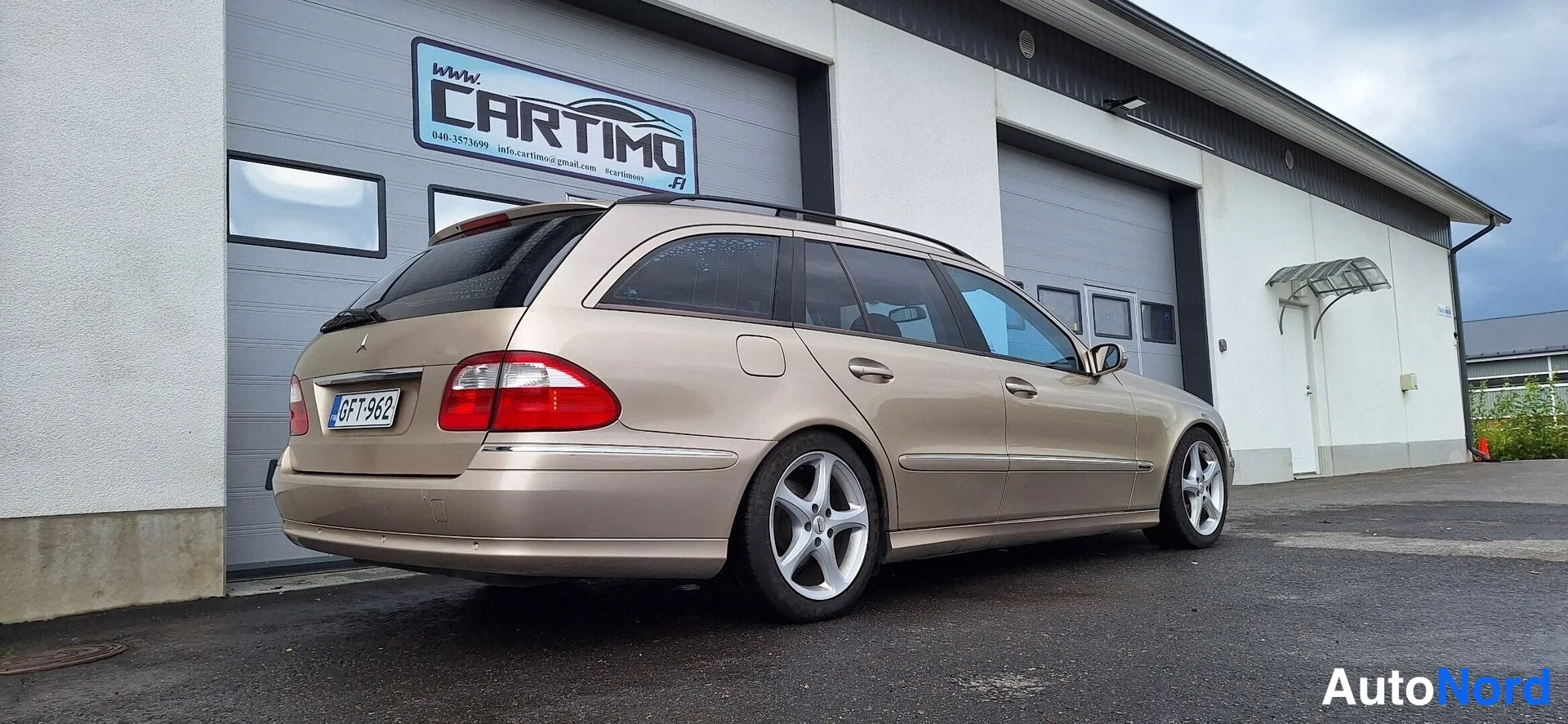 Takaviisto: Beige Mercedes-Benz farmarista takaa sivulta kuvattuna; näkyvissä takavalot, takapuskuri ja rekisteritunnus, kattokaiteet ja hopeiset kevytmetallivanteet.