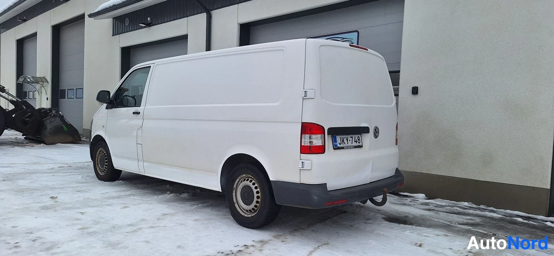 Takaviisto: Valkoinen pakettiauto takaa kulmasta talvisessa pihamaastossa.
