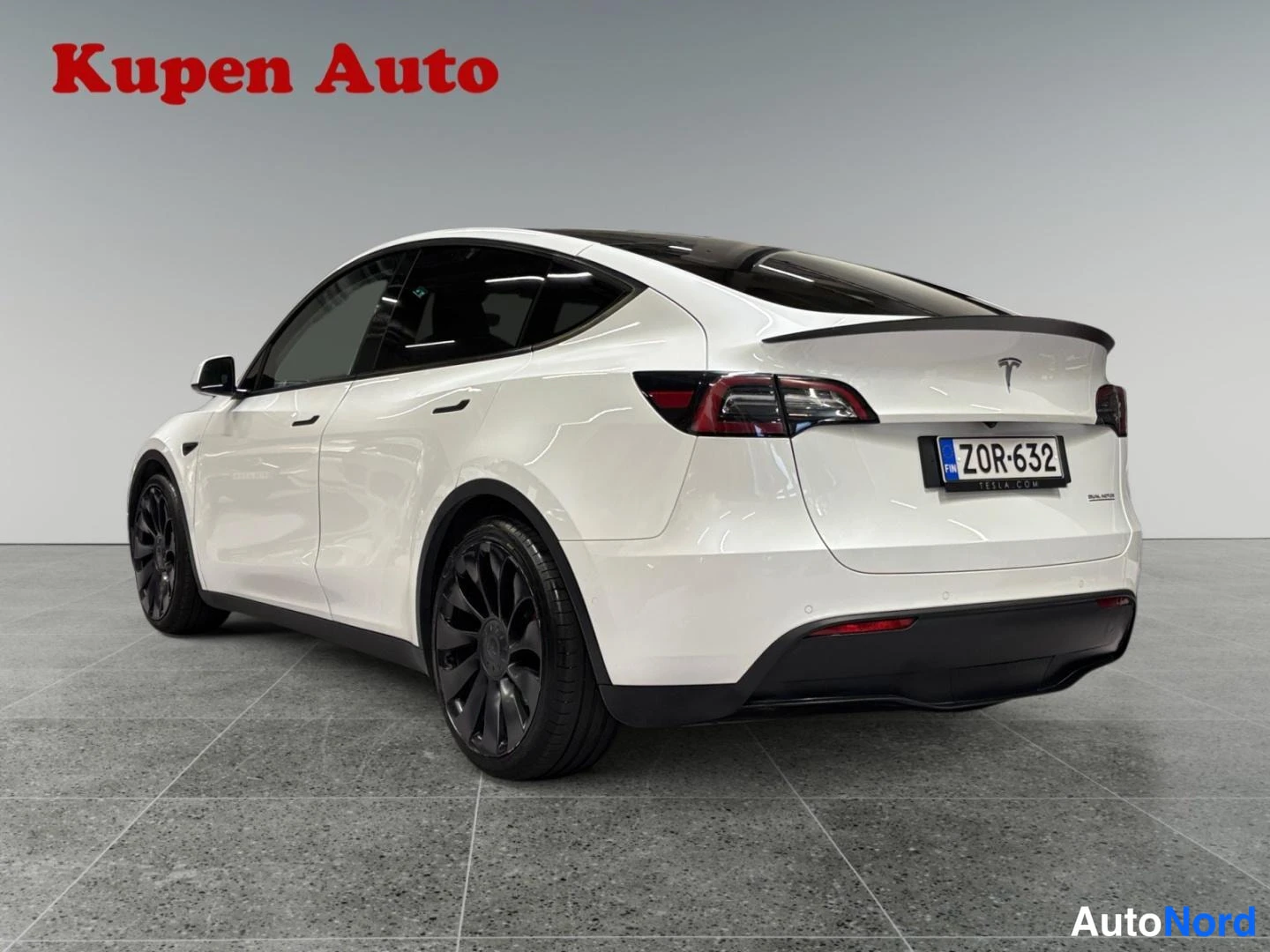 Takaviisto: Valkoinen Tesla Model Y takakulmasta vasemmalta, takavalot ja rekisterikilpi näkyvissä, mustat pyörät.