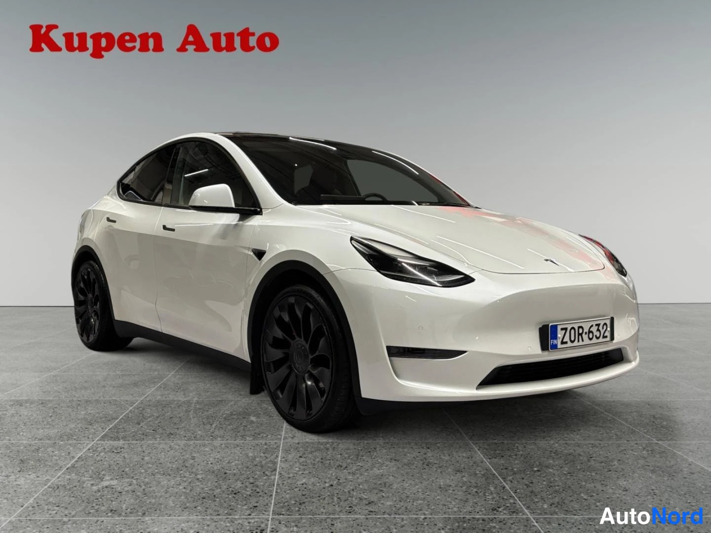 Etuviisto, nokka oikealle: Valkoinen Tesla Model Y etukulmasta oikealta, rekisterikilpi, tummat kevytmetallivanteet ja tumma lasikatos.