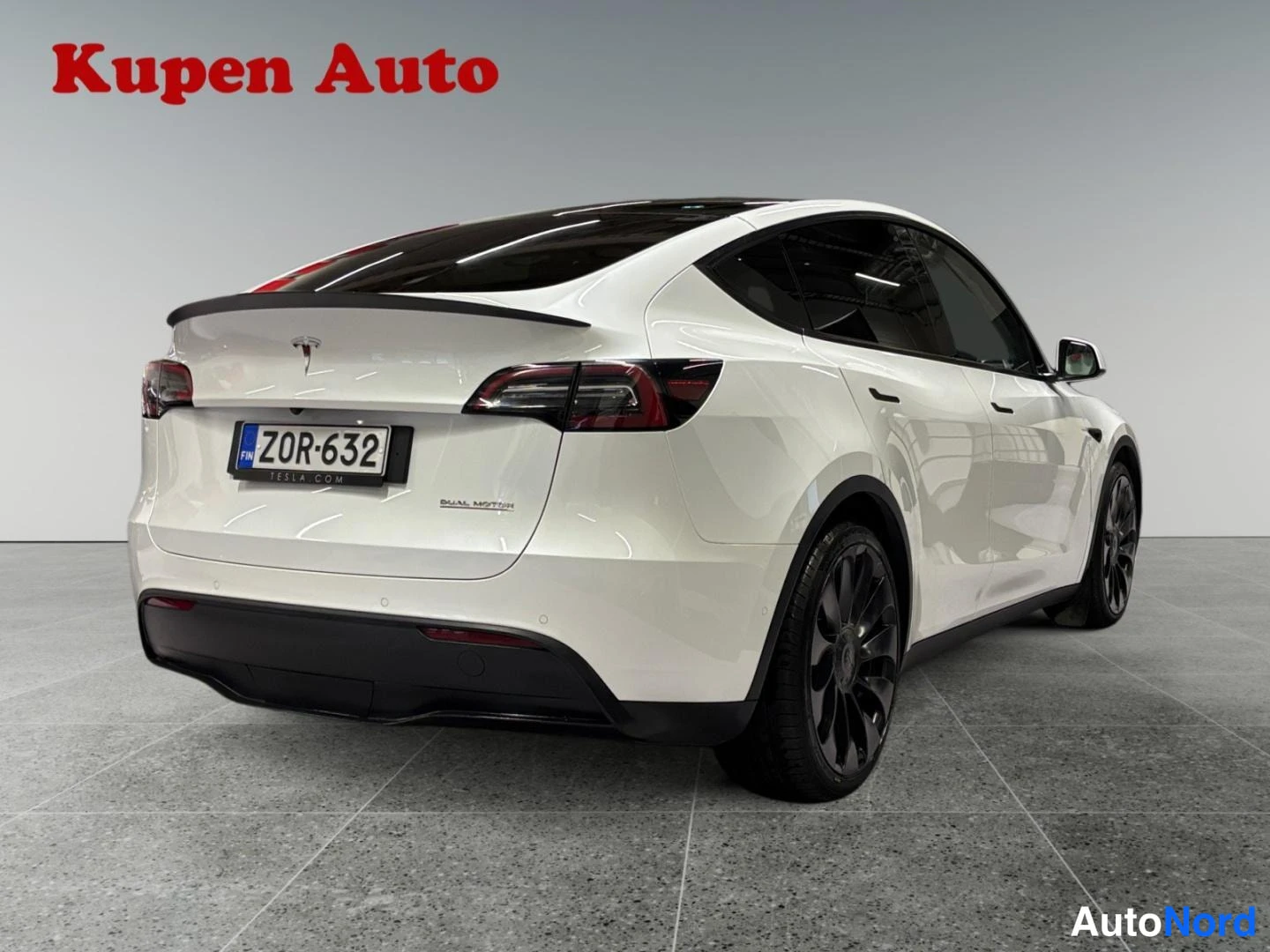 Takaviisto: Valkoinen Tesla Model Y takakulmasta oikealta, tavaratilan kansi ja takavalot näkyvissä, rekisterikilpi.