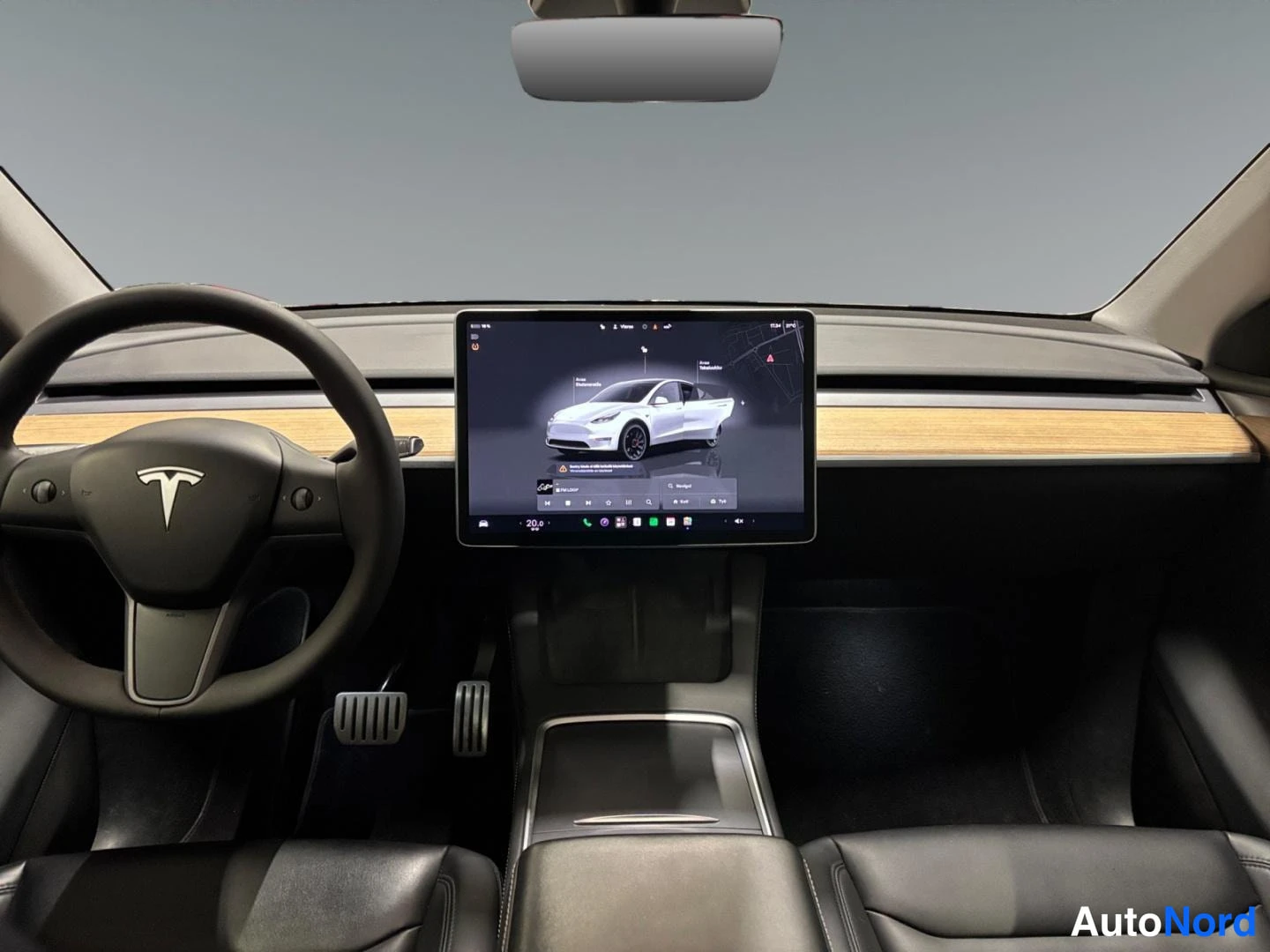 Muu: Tesla-automallin ohjaamo nähtynä kuljettajan paikalta: ohjauspyörä, keskitörmällä suuri kosketusnäyttö ja mustat penkit.