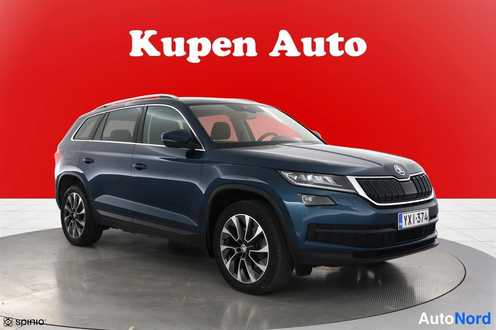 Etuviisto, nokka oikealle: Sininen Skoda Kodiaq -maasturi etu‑kolmannesvasemmalta kuvattuna studioympäristössä, punainen tausta.
