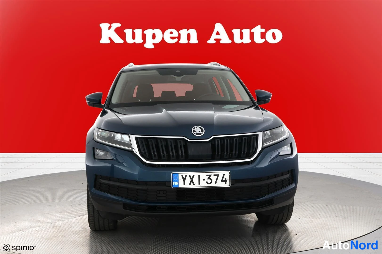 Edestä: Sininen Skoda Kodiaq suoraan edestä kuvattuna, rekisterikilpi, punainen tausta.